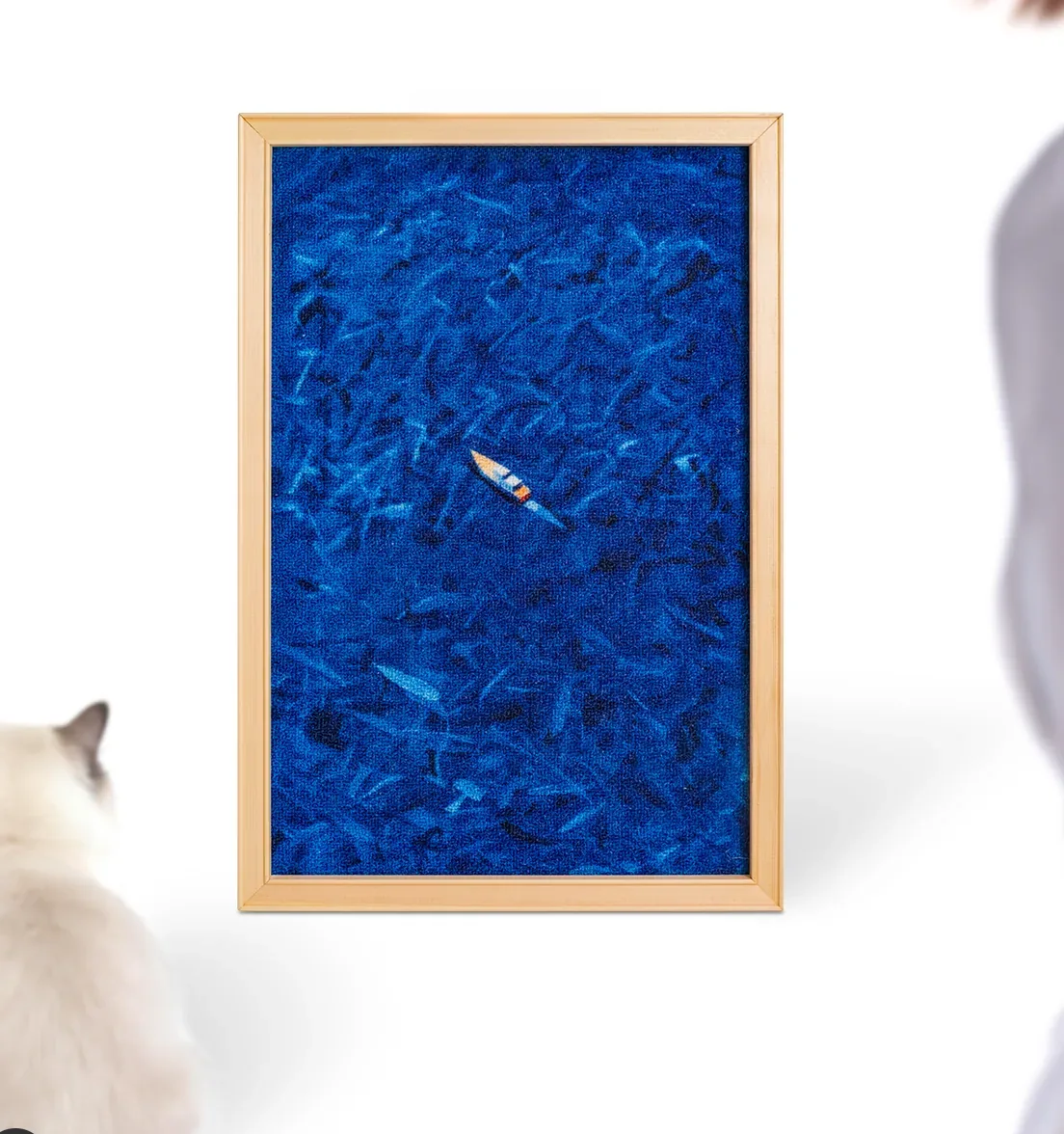 A white cat inspecting the Wave Light print, a tiny boat on a deep blue sea