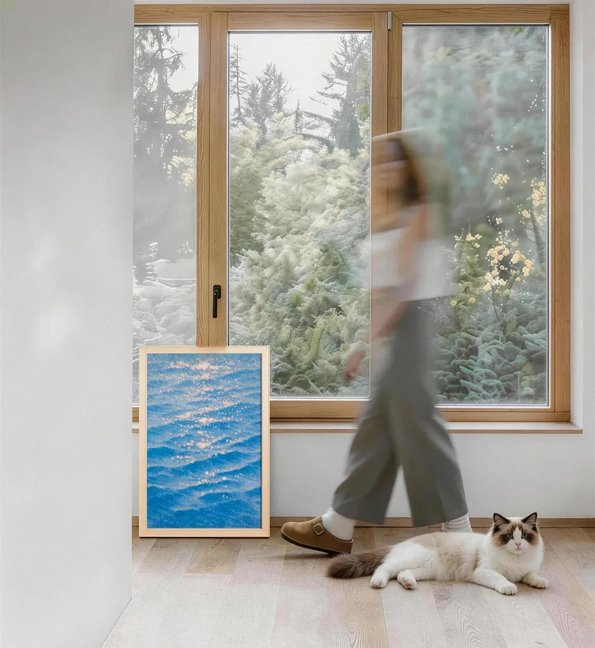 A person walks past a window, a cat rests beside the leaning canvas
